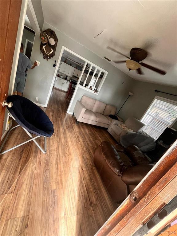 living area featuring baseboards, lofted ceiling, wood finished floors, and a ceiling fan