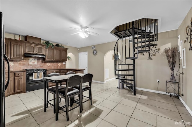 kitchen with dark brown cabinetry, ceiling fan, black gas range oven, decorative backsplash, and light tile patterned floors