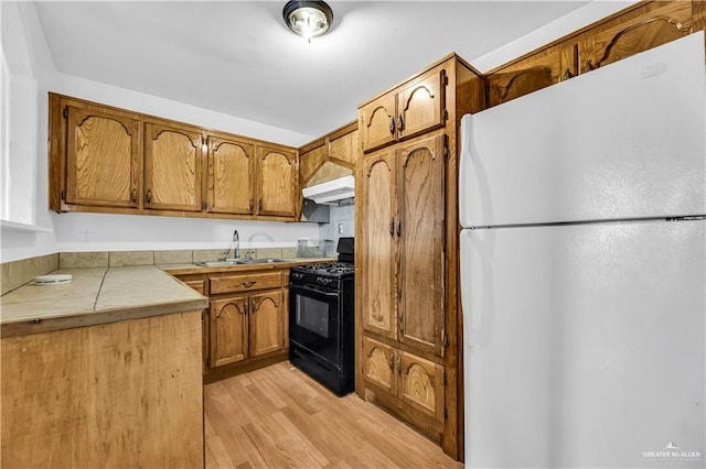 kitchen with sink, black range with gas stovetop, white fridge, light hardwood / wood-style floors, and custom exhaust hood