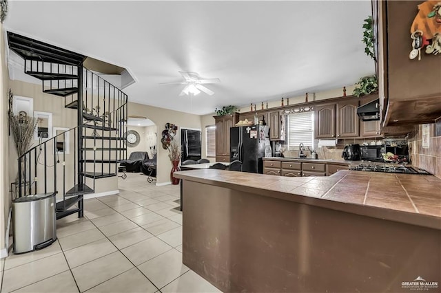 kitchen featuring dark brown cabinetry, ceiling fan, tile countertops, decorative backsplash, and black appliances