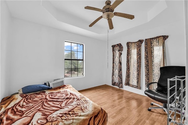 bedroom with hardwood / wood-style floors, ceiling fan, a wall unit AC, and a tray ceiling