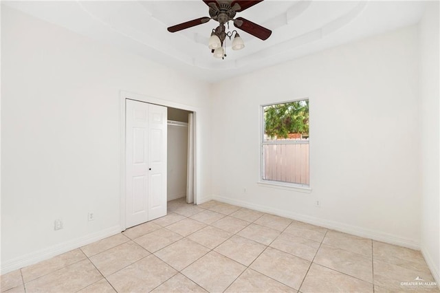 unfurnished bedroom featuring a closet, a raised ceiling, ceiling fan, and light tile patterned flooring