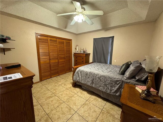 tiled bedroom featuring a textured ceiling, a closet, a raised ceiling, and ceiling fan