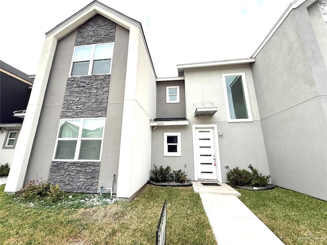 view of front facade featuring a front yard, stone siding, and stucco siding