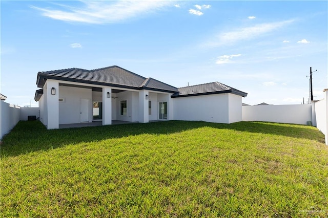 rear view of property featuring a yard, a tiled roof, a fenced backyard, and stucco siding