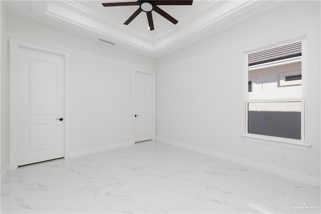 spare room with ceiling fan, marble finish floor, a tray ceiling, and visible vents