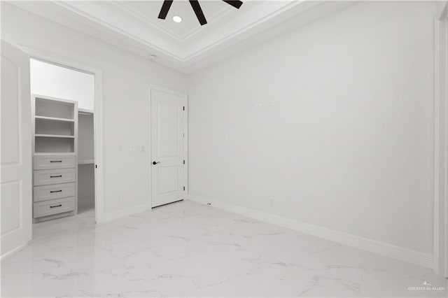 unfurnished bedroom featuring crown molding, a ceiling fan, a spacious closet, marble finish floor, and baseboards