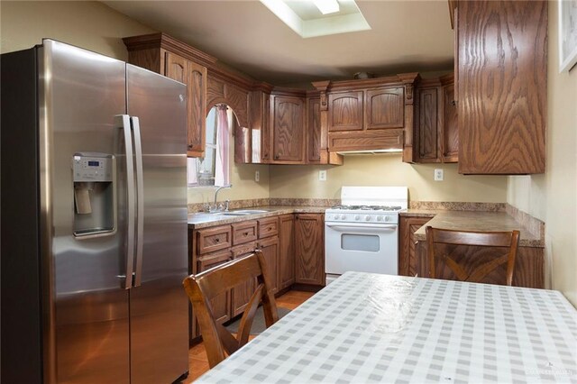 kitchen featuring white gas range, light tile patterned flooring, stainless steel fridge with ice dispenser, and sink