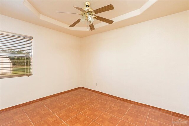 empty room with ceiling fan and a raised ceiling