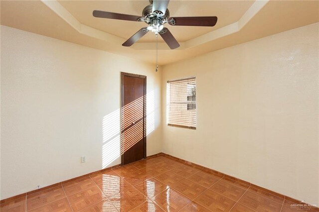 unfurnished room featuring a tray ceiling, tile patterned floors, and ceiling fan