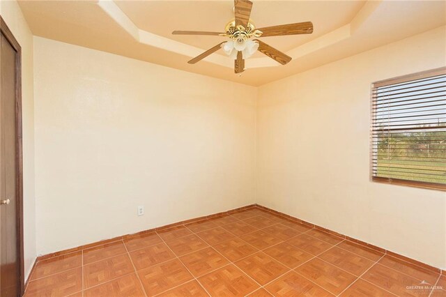 tiled empty room with a raised ceiling and ceiling fan