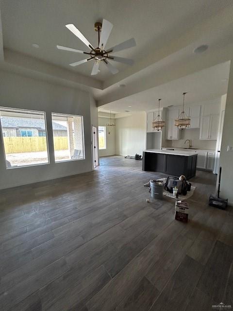 unfurnished living room featuring sink, a tray ceiling, dark hardwood / wood-style floors, and ceiling fan