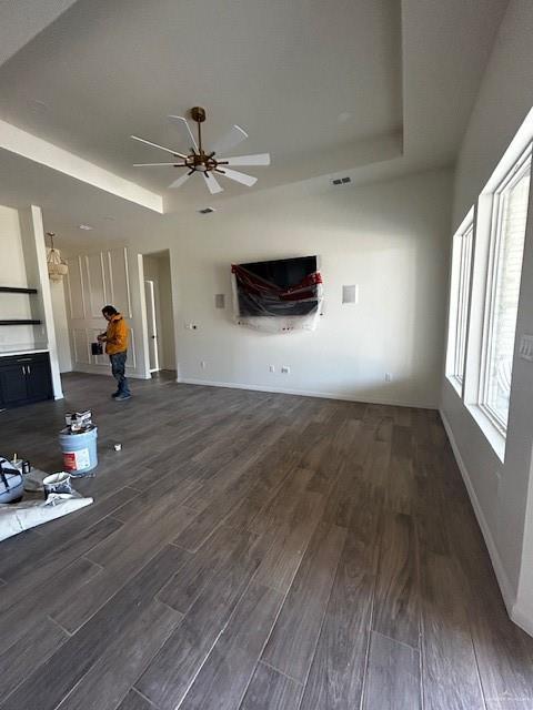 unfurnished living room featuring ceiling fan, a tray ceiling, and dark hardwood / wood-style flooring