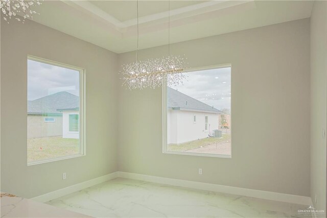 unfurnished dining area featuring marble finish floor, baseboards, a tray ceiling, and an inviting chandelier