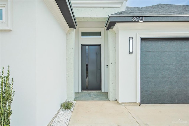 view of exterior entry featuring roof with shingles, an attached garage, stucco siding, and elevator