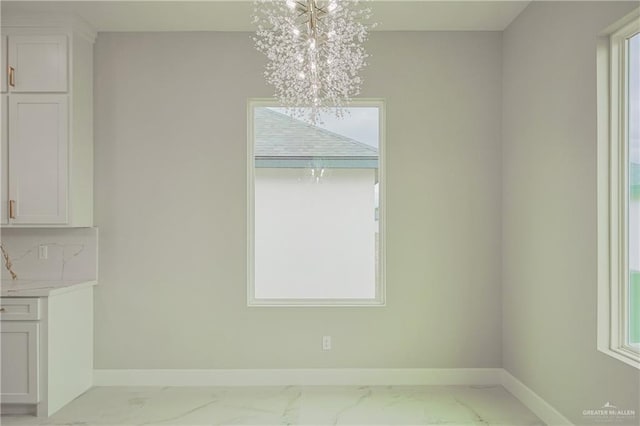 unfurnished dining area with a chandelier, marble finish floor, plenty of natural light, and baseboards