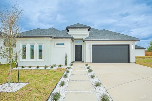 prairie-style house with a garage, a shingled roof, concrete driveway, a front yard, and stucco siding