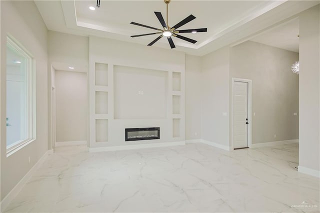 unfurnished living room featuring a glass covered fireplace, marble finish floor, a raised ceiling, and baseboards