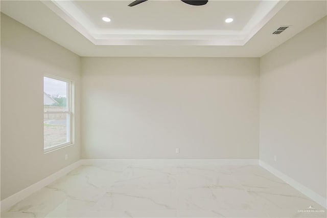 empty room featuring marble finish floor, visible vents, a tray ceiling, and baseboards