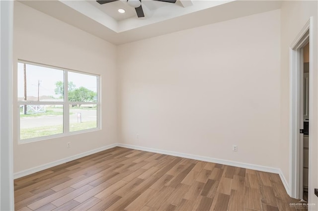 empty room featuring a ceiling fan, baseboards, light wood-style flooring, and a tray ceiling