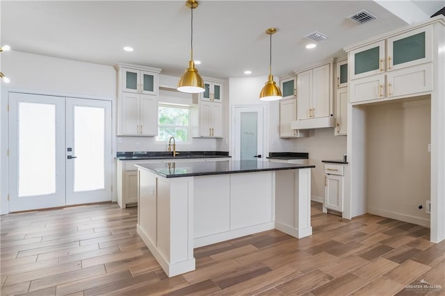 kitchen with a center island, under cabinet range hood, light wood-style flooring, and visible vents
