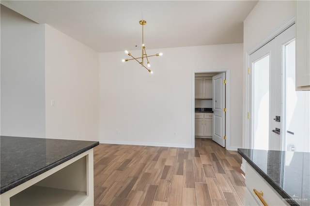 unfurnished dining area featuring baseboards, light wood-style flooring, and a chandelier