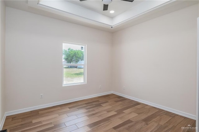 spare room with a ceiling fan, baseboards, a raised ceiling, and light wood-type flooring