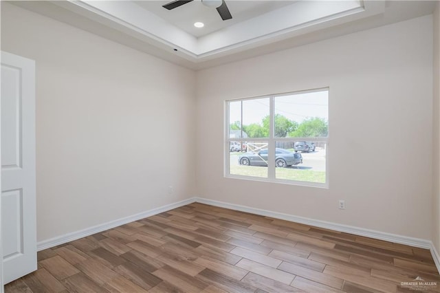 unfurnished room featuring baseboards, a raised ceiling, ceiling fan, and wood finished floors