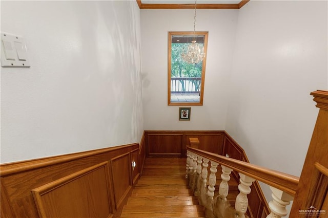 staircase featuring hardwood / wood-style flooring, ornamental molding, and a notable chandelier