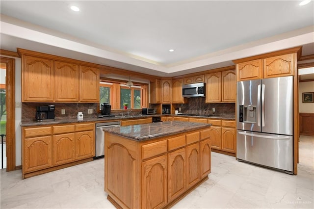 kitchen with tasteful backsplash, stainless steel appliances, sink, dark stone countertops, and a kitchen island