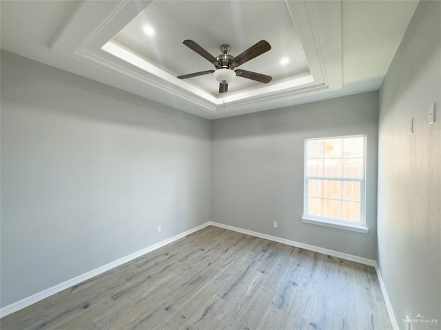 spare room with a tray ceiling, ceiling fan, and light wood-type flooring