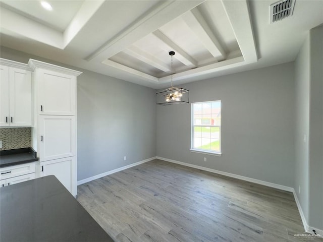 unfurnished dining area featuring a tray ceiling, a notable chandelier, and light wood-type flooring