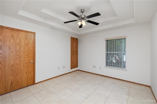 spare room featuring light tile patterned floors, visible vents, a ceiling fan, baseboards, and a raised ceiling