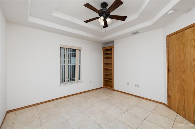 spare room with a tray ceiling, visible vents, light tile patterned flooring, ceiling fan, and baseboards