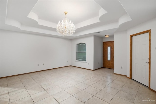 spare room featuring a chandelier, a raised ceiling, light tile patterned flooring, and baseboards