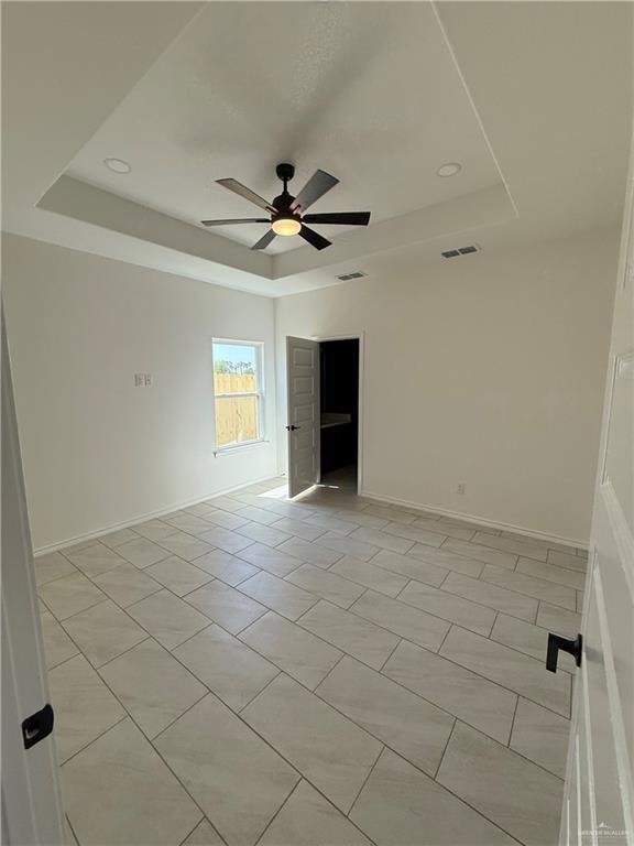 unfurnished room with a ceiling fan, baseboards, visible vents, a tray ceiling, and light tile patterned flooring