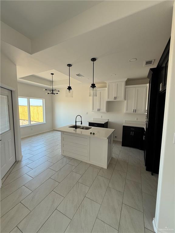 kitchen featuring a sink, visible vents, a raised ceiling, and a center island with sink