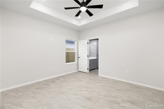 spare room with baseboards, a raised ceiling, and ceiling fan