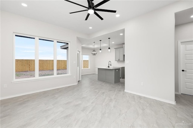 unfurnished living room featuring a ceiling fan, recessed lighting, baseboards, and a sink