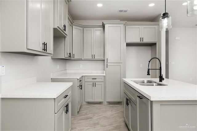 kitchen featuring visible vents, gray cabinetry, a kitchen island with sink, pendant lighting, and a sink