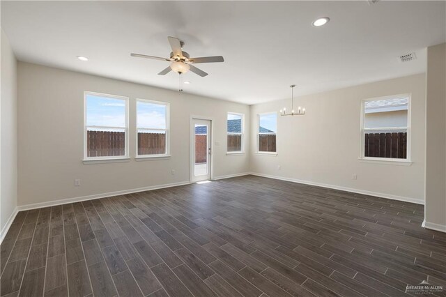 unfurnished living room with ceiling fan with notable chandelier, visible vents, dark wood-type flooring, and a healthy amount of sunlight