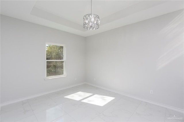 spare room featuring a raised ceiling and a notable chandelier