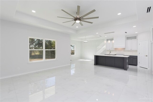 kitchen featuring decorative light fixtures, white cabinets, a raised ceiling, and a kitchen island with sink