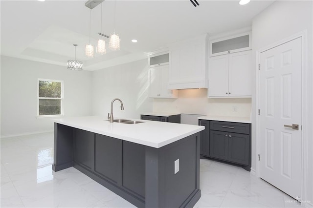 kitchen featuring a raised ceiling, a kitchen island with sink, pendant lighting, white cabinets, and sink