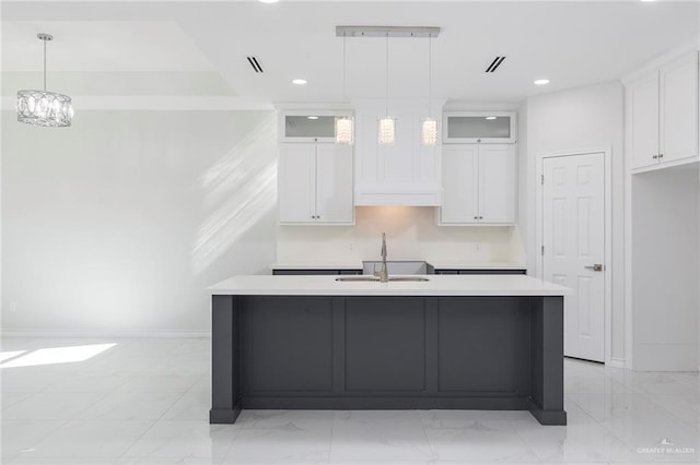 kitchen with a center island with sink, pendant lighting, white cabinets, and sink