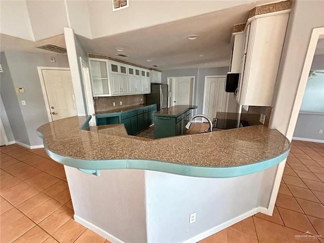 kitchen with a kitchen island, stainless steel fridge, white cabinets, light tile patterned floors, and kitchen peninsula