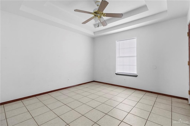 tiled empty room featuring ceiling fan and a raised ceiling