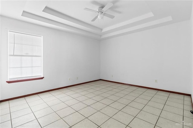 empty room featuring a tray ceiling, ceiling fan, and light tile patterned floors