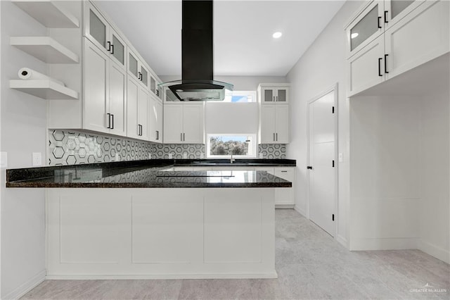 kitchen with a peninsula, dark stone counters, white cabinets, and island exhaust hood
