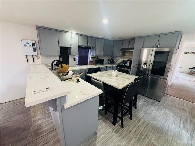 kitchen featuring a peninsula, gray cabinetry, tasteful backsplash, and stainless steel fridge with ice dispenser